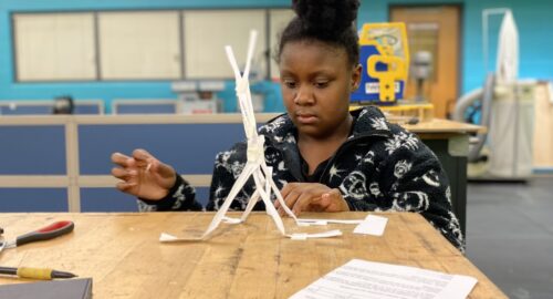 Female design and modeling student working on a paper tower challenge in classroom