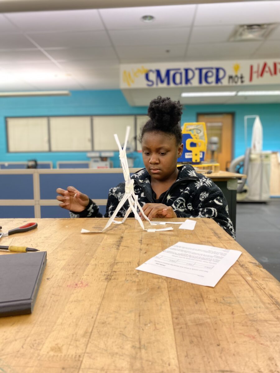 Female design and modeling student working on a paper tower challenge in classroom