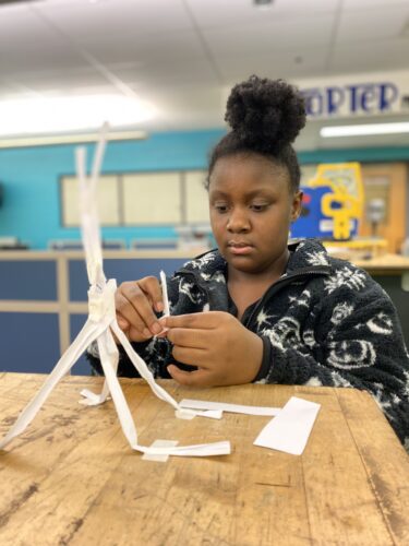A female design and modeling student working on her paper tower challenge 